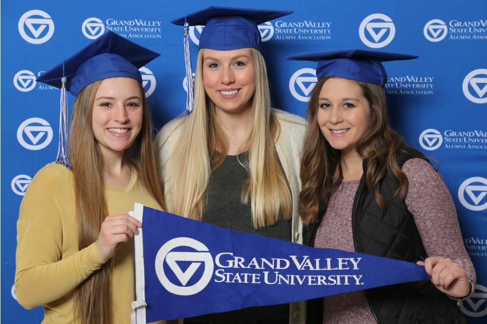 Three graduates pose with GV flag at Gradfest